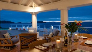 Eine Terrasse mit Meerblick, ausgestattet mit Korbmöbeln, einem für ein Essen gedeckten Tisch und einer Kerze.