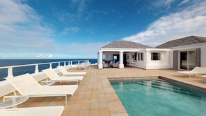 A poolside area with lounge chairs, a pool, and a covered seating area with a view of the ocean. - Cap Au Vent Luxury villa (Pointe Milou)