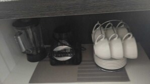 Een kitchenette met een koffiezetapparaat, een blender en een rek voor mokken.
