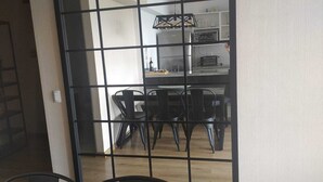 Een eethoek met een tafel en stoelen, een keuken op de achtergrond, en een rasterachtig scheidingswand.