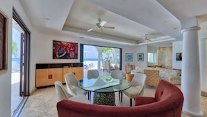 A modern living room with a glass-top dining table, red velvet chairs, and a view of the ocean. - Beautiful Bahari Luxury villa (Simpson Bayv)