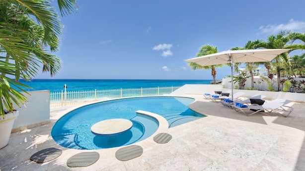 A pool with a curved design, surrounded by lounge chairs and umbrellas, with a view of the ocean. - Beautiful Bahari Luxury villa (Simpson Bayv)