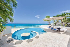 A pool with a curved design, surrounded by lounge chairs and umbrellas, with a view of the ocean. - Beautiful Bahari Luxury villa (Simpson Bayv)