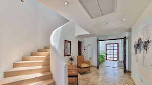 A spacious hallway with a curved staircase, a wicker chair, and a door leading to a balcony. - Beautiful Bahari Luxury villa (Simpson Bayv)