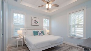 A bedroom with a bed, two bedside tables, a ceiling fan, and large windows with blinds. - New!! Steps To Beach, Gulf Views, Private Heated Pool (Panama City Beach)