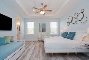 Een slaapkamer met een bed, een witte dressoir, een plafondventilator en een aan de muur bevestigde televisie.