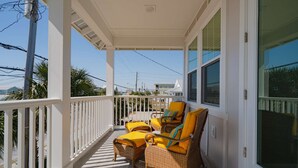 A covered porch with wicker furniture and yellow cushions, overlooking a residential area. - New!! Steps To Beach, Gulf Views, Private Heated Pool (Panama City Beach)