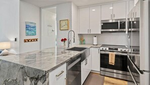 Una cucina moderna con mobili bianchi, elettrodomestici in acciaio inossidabile, un piano di lavoro in marmo e decorazioni a parete.