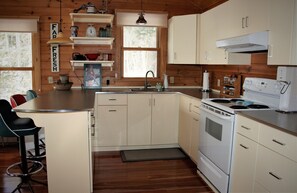 Una cocina con armarios de madera, estufa, lavaplatos y un comedor con sillas.