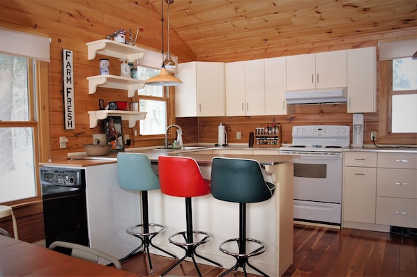 A kitchen with wooden cabinets, a stove, a sink, and bar stools.