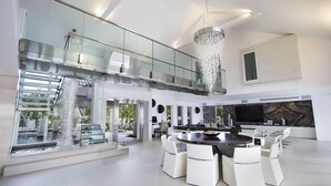 Un intérieur spacieux et moderne, avec un coin repas central, un grand lustre et une vue sur un élément décoratif aquatique.