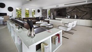 Un salon moderne doté d’un grand canapé en forme de L, d’une table basse en verre et d’un coin cuisine avec un pare-feu en marbre et un téléviseur à écran plat.