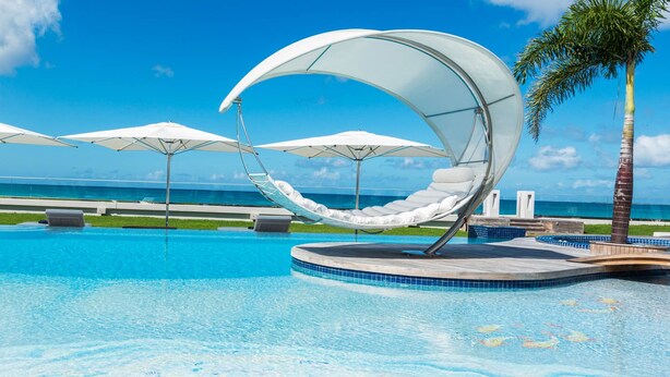 Une piscine à bords arrondis, des parasols blancs et des chaises longues.