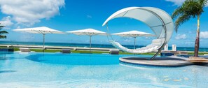 Una piscina con borde circular, sombrillas blancas y sillas de descanso.