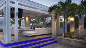 Un espace de vie extérieur moderne, doté d’une structure blanche, d’un canapé et d’un escalier menant à une terrasse.