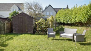 A backyard with a wooden shed, two wicker chairs, and a hedge.