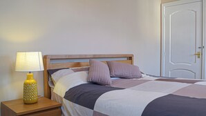 A neatly made bed with a wooden headboard, a bedside table with a lamp, and a door in the background.