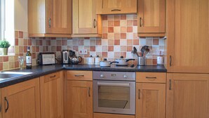 A kitchen with wooden cabinets, a toaster, a kettle, a coffee maker, and a stove. - 3 bedroom accommodation in Marloes (Marloes)