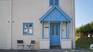 A building with a blue door and window frames, a small porch with two chairs, and a chimney. - 3 bedroom accommodation in Marloes (Marloes)