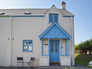 Un bâtiment avec une porte et des encadrements de fenêtres bleus, un petit porche avec deux chaises et une cheminée.