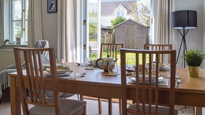 A dining area with a wooden table set for four, chairs, and a view of a garden and house through an open door. - 3 bedroom accommodation in Marloes (Marloes)