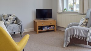 A living room with a television on a wooden cabinet, a window with curtains, and two armchairs with patterned cushions. - 3 bedroom accommodation in Marloes (Marloes)