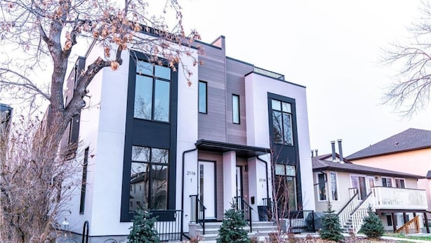 A modern two-story house with large windows, a front porch, and a small front yard with a tree and a Christmas tree. - Executive home, Rooftop Deck, close to Foothills Med Ctr, Kensington Plaza & DT (Calgary)