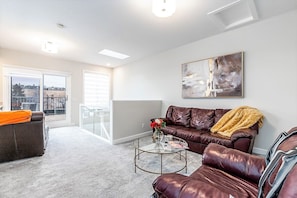 A modern living room with a leather sofa, a coffee table, and a large window with a view of a cityscape.
