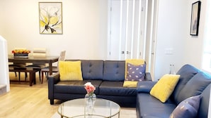 A modern living room with a dark blue sofa, a glass coffee table, and a dining area with a white table and chairs. - Executive home, Rooftop Deck, close to Foothills Med Ctr, Kensington Plaza & DT (Calgary)