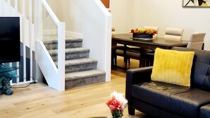A modern living room with a staircase, a dining area, and a sofa with a yellow pillow. - Executive home, Rooftop Deck, close to Foothills Med Ctr, Kensington Plaza & DT (Calgary)