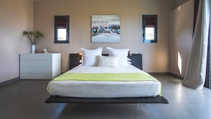 Een moderne slaapkamer met een groot bed, een nachtkastje, een wandlamp en een raam met gordijnen.
