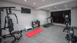 Een huisgymnasium met een loopband, elliptische trainer, gewichtbank en diverse fitnessapparaten.