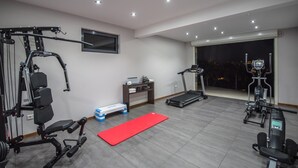 Un gimnasio en casa con cinta de correr, elíptica, banco de pesas y diversas máquinas de ejercicio.