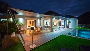 Un espacio exterior moderno con piscina, terraza de madera y zona de estar cubierta.