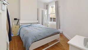 A bedroom with a bed, a nightstand, a wardrobe, and a window with curtains.