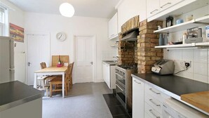 A modern kitchen with white cabinetry, a brick oven, and a dining area with a wooden table and chairs.