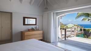 A bedroom with a bed, a wooden dresser, a mirror, and a view of the ocean and a deck. - Bijou (1/2 Rooms) Luxury villa (Flamands)