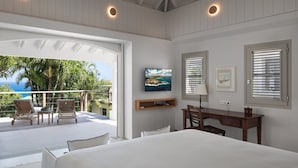 A bedroom with a large bed, a desk, and a chair. There is a balcony with chairs and a view of the ocean. - Bijou (1/2 Rooms) Luxury villa (Flamands)