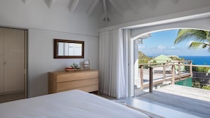 A bedroom with a bed, a wooden dresser, a mirror, and a view of the ocean and a deck. - Beautiful Bijou Luxury villa (Flamands)