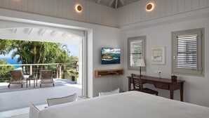 A bedroom with a large bed, a desk, and a chair. There is a balcony with chairs and a view of the ocean. - Beautiful Bijou Luxury villa (Flamands)