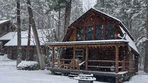 A wooden cabin with a porch, surrounded by snow-covered trees. - Rustic MT Cabin (Kalispell)