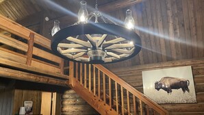 A wooden staircase with a chandelier, a framed bison picture, and a Glacier National Park sign. - Rustic MT Cabin (Kalispell)