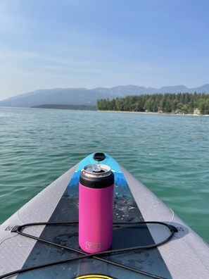 A kayak with a pink water bottle labeled 'YETI' on its side, a blue paddle, and a view of calm water with distant mountains and a forested shoreline. - Rustic MT Cabin (Kalispell)