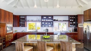 A modern kitchen with wooden cabinets, a central island with chairs, a built-in oven, and a large window. - Bellissima (2/3 Rooms) (Gouverneur)