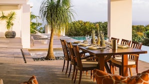 An outdoor dining area with a table set for six, surrounded by chairs, near a pool and palm tree. - Bellissima (2/3 Rooms) (Gouverneur)
