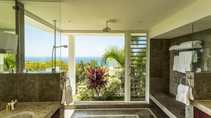 Une salle de bain moderne dotée d’une grande porte vitrée donnant sur un balcon, d’une douche et d’un meuble-lavabo avec un miroir.