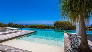 Une piscine d’un bleu éclatant, dotée d’une terrasse en bois, entourée de rochers et d’un palmier.
