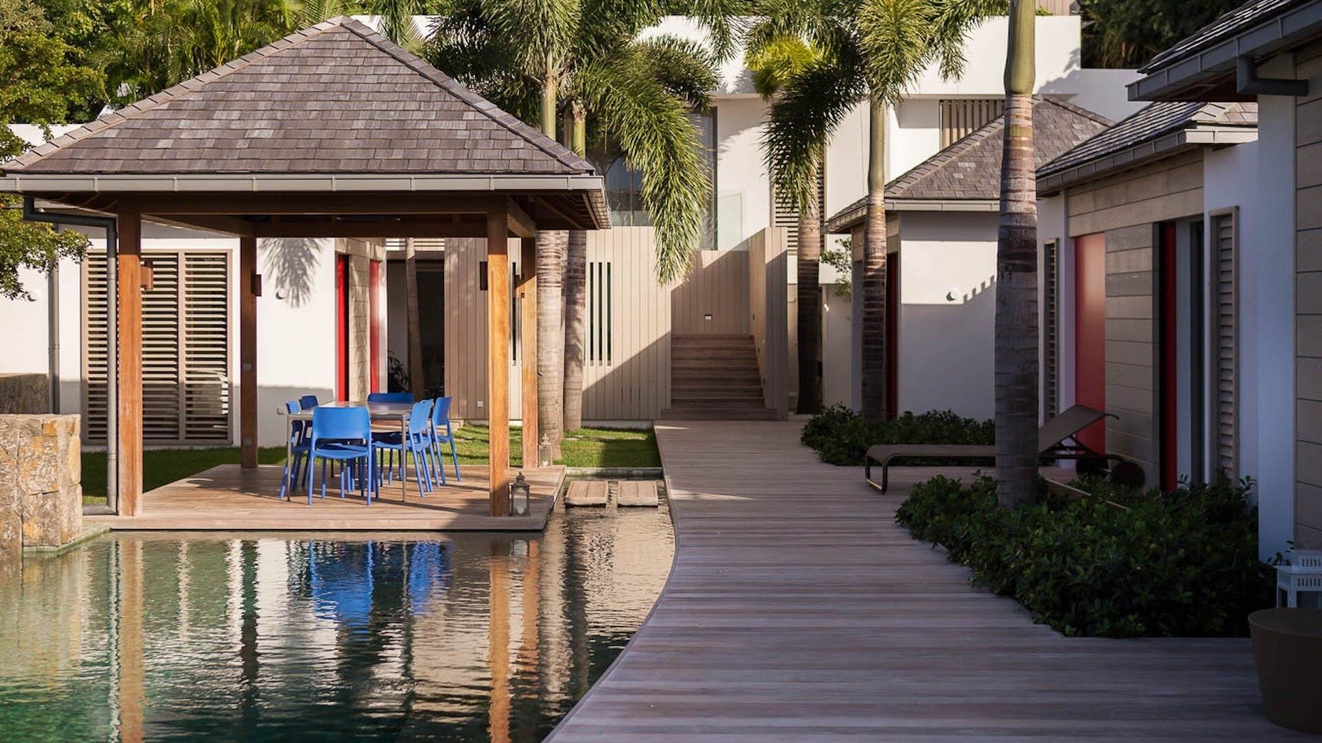 Un espace piscine agrémenté d’un gazebo, de chaises bleues et d’une terrasse en bois.