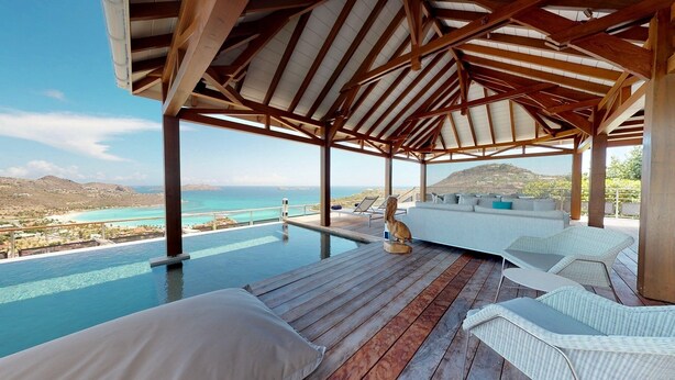 An infinity pool with a wooden deck, white wicker furniture, and a view of the ocean and hills. - W View (1/4 Rooms) Luxury villa (Saint Jean)