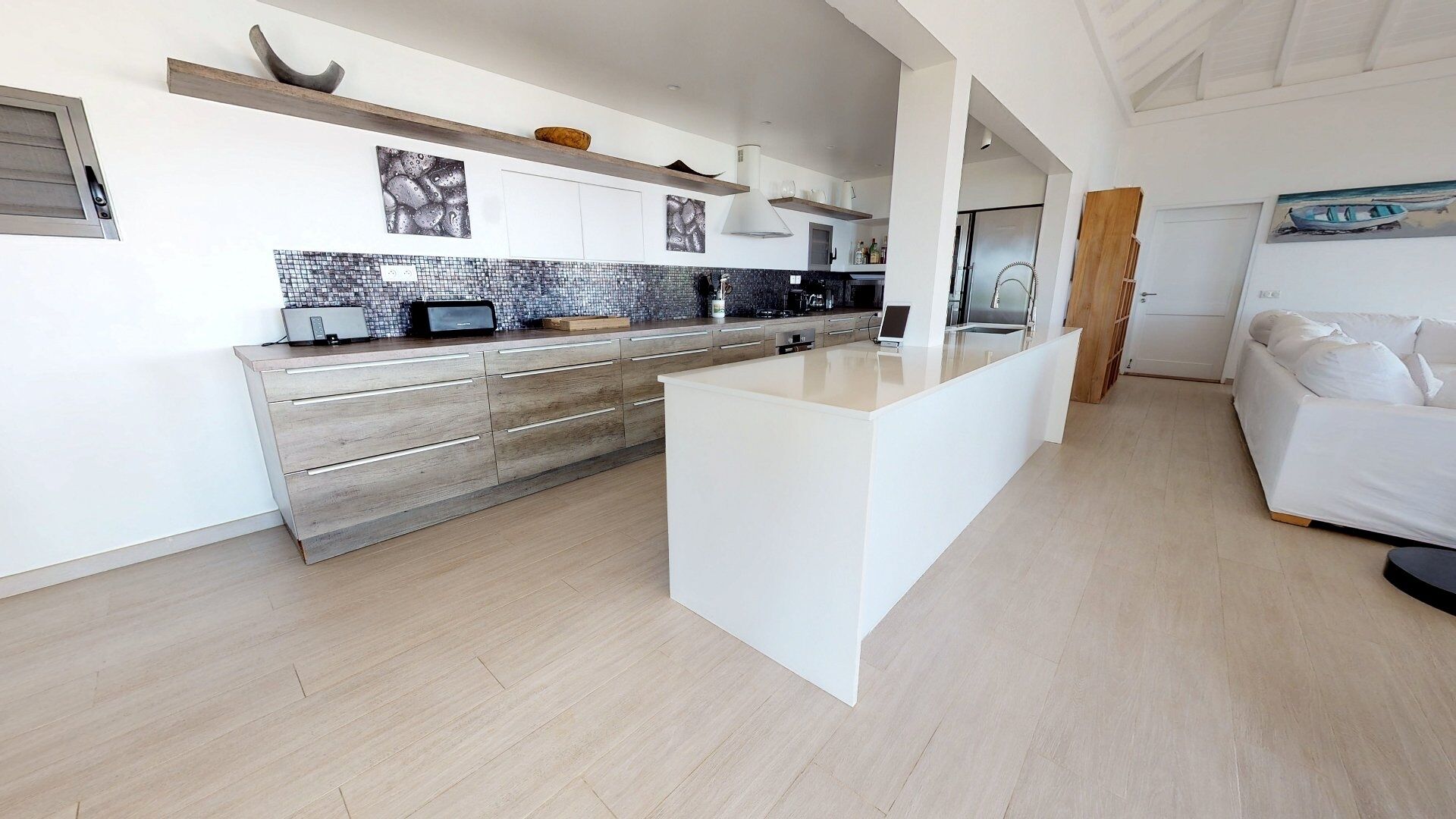 A modern kitchen with wooden cabinets, a central island, and a dining area with a white sofa.